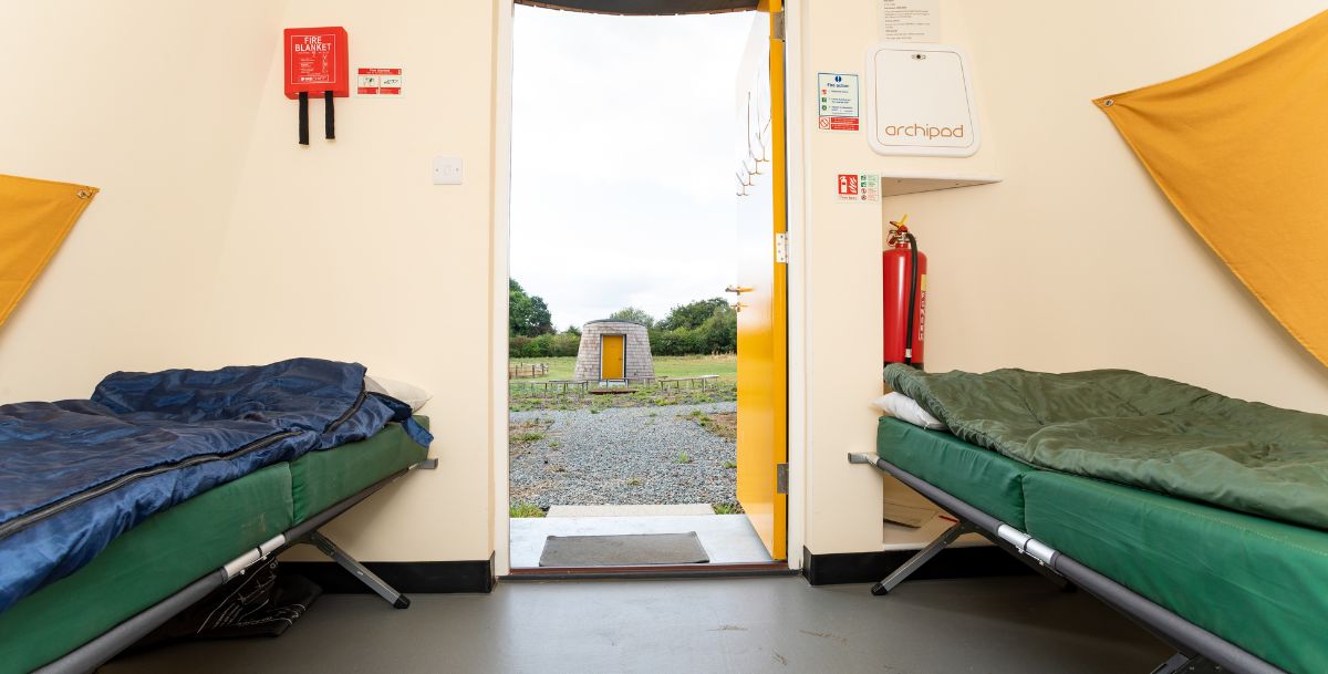 Two camp beds with a open door and view of the pods 