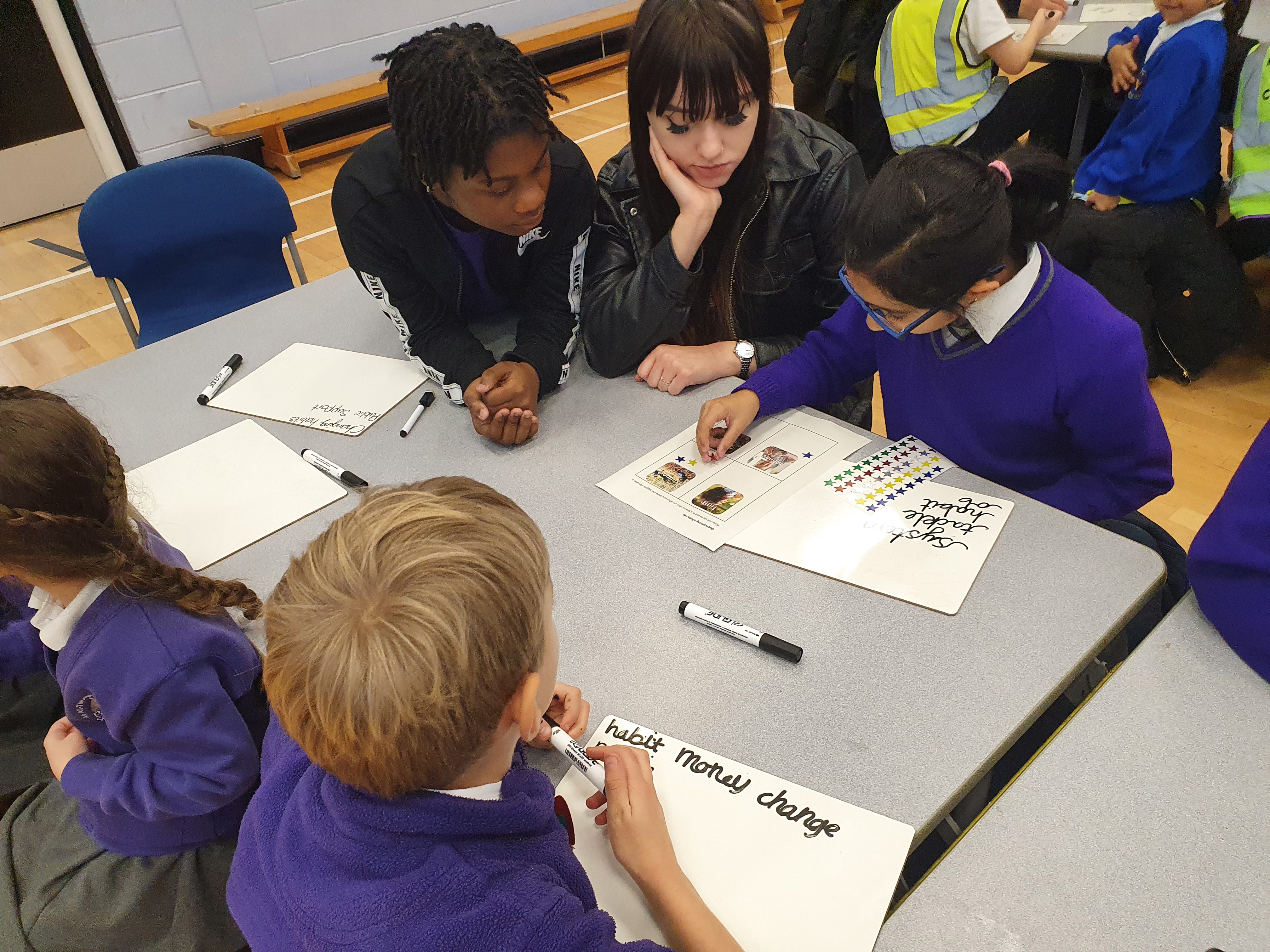 A teenage girl sits with a group of primary school children helping them work 