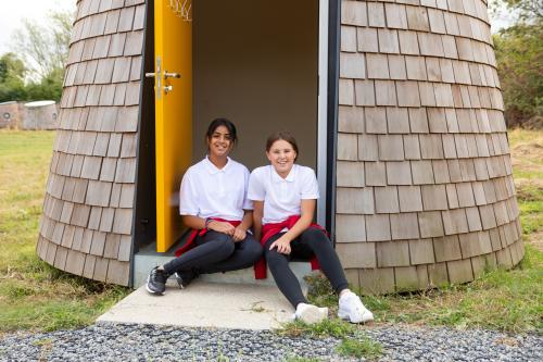 Two schoolgirls sitting outside hut