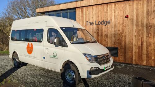 image of a large white minibus in front of a wooden building named 'the lodge'