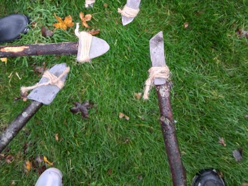 an image of diy stone age spears, wooden sticks with flint arrows attached by string, all pointing towards each other with a grassy background